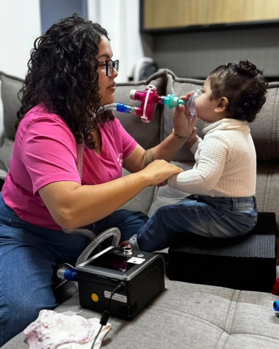 Fisioterapeuta realizando fisioterapia respiratória infantil em bebê, no colo.