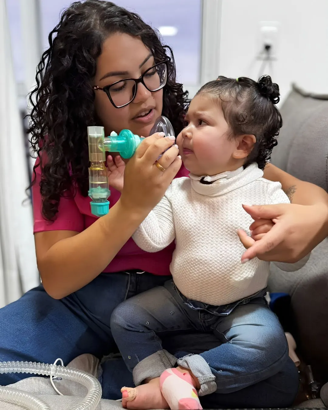 Criança recebendo fisioterapia respiratória com máscara, em atendimento domiciliar.