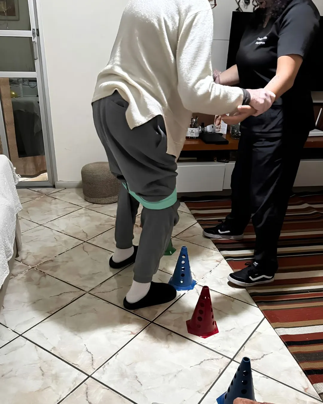 Paciente adulto em treino de equilíbrio com cones, acompanhado pela fisioterapeuta.