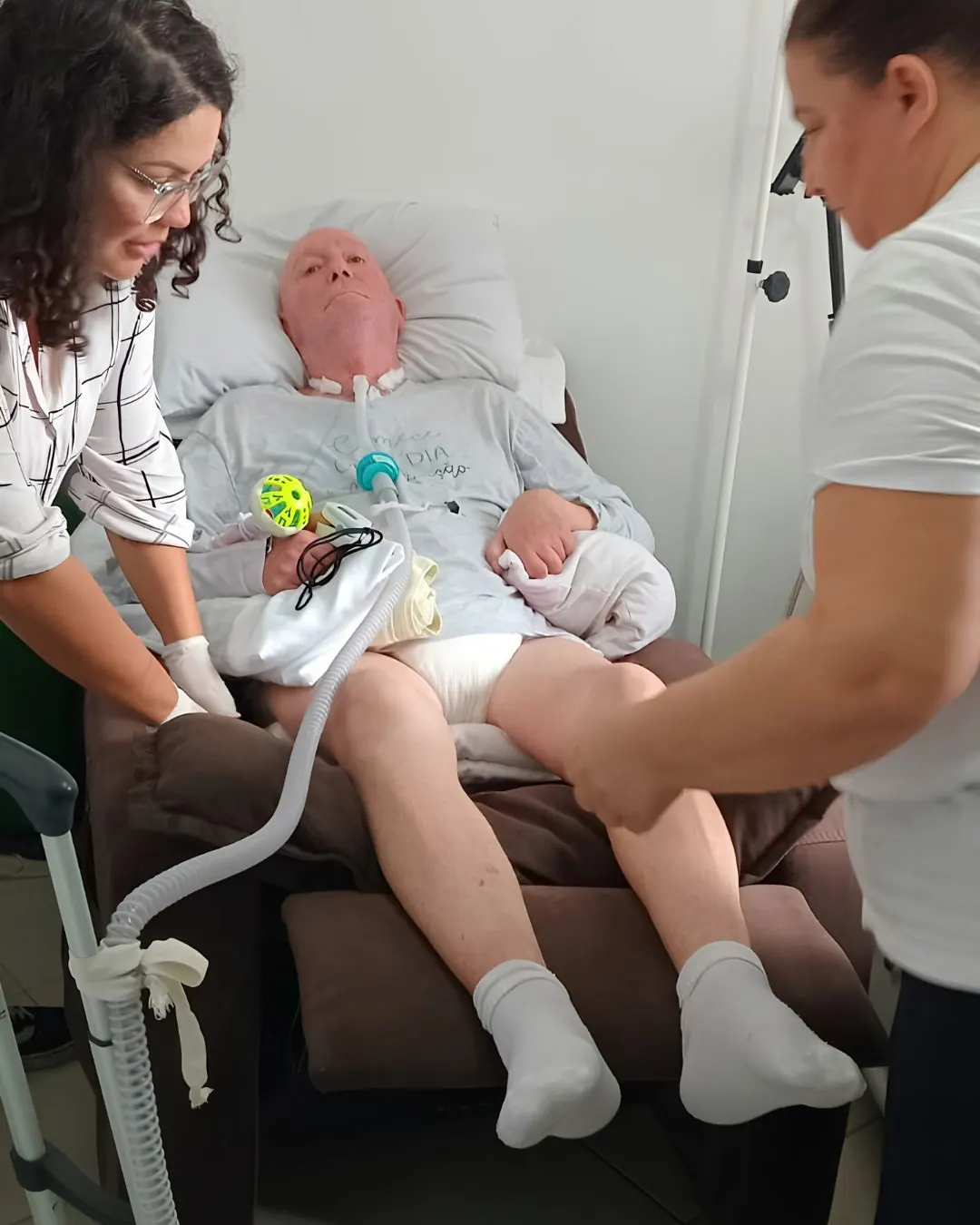 Fisioterapeuta atendendo paciente idoso em casa, com bebê por perto durante a sessão.